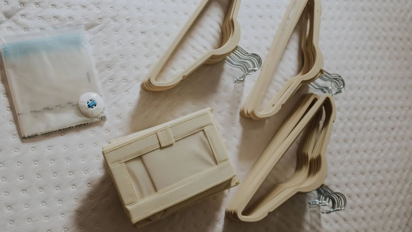 A neatly arranged flat lay of beige wooden hangers and a fabric storage box on a quilted surface.