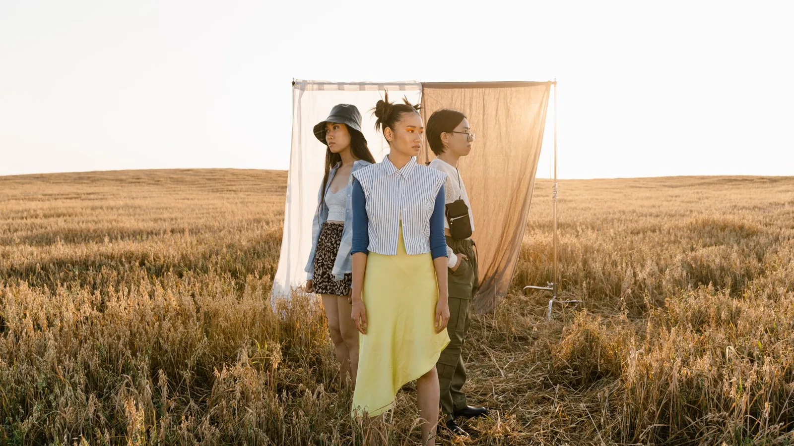 Three stylish women stand in a field, showcasing modern fashion amidst a serene outdoor backdrop.