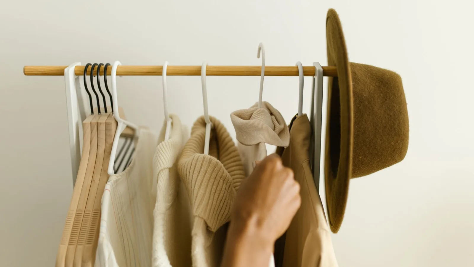 Stylish beige and brown clothes on a rack with a hand reaching in.