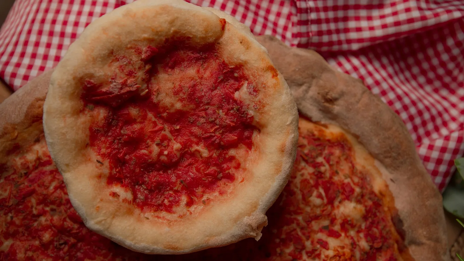 Close-up of rustic homemade pizzas with fresh tomato sauce on a checkered tablecloth.