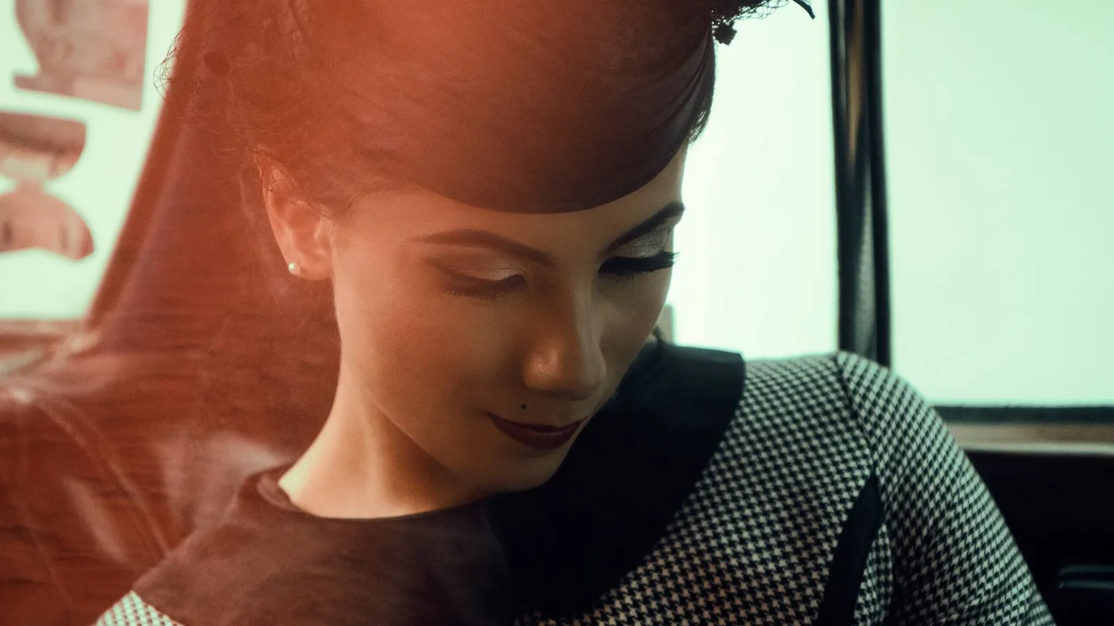 Elegant woman in vintage attire posing inside a car with a graceful expression.